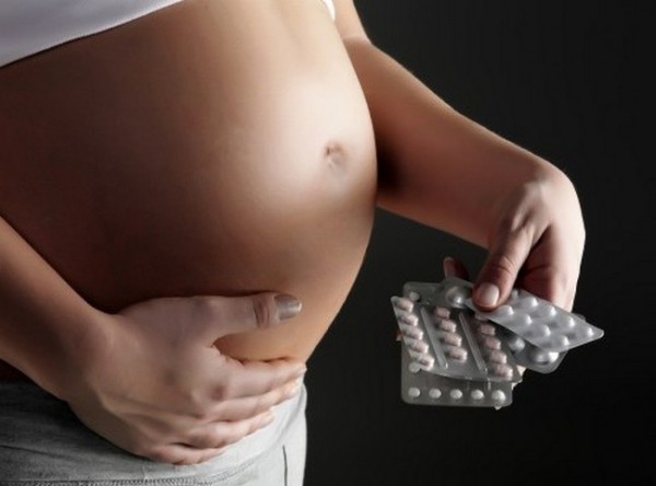 Беременная женщина держит в руках таблетки