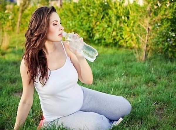 Беременная пьёт воду из пластиковой бутылки