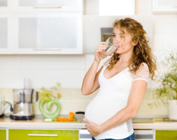 Беременная женщина пьёт из стакана