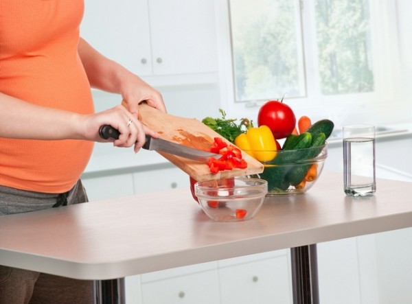 Беременная женщина нарезает овощи на кухне